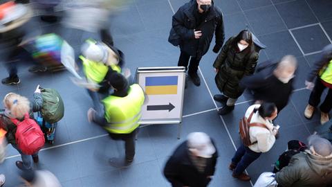 Eine Szene am Berliner Hauptbahnhof aus der Vogelperspektive: Ankunft geflüchteter Menschen aus der Ukraine am 12.3.22. Es gibt ein Hinweisschild mit der ukrainischen Flagge und einem Pfeil. Viele Menschen, manche mit Koffern, einige mit Warnwesten.