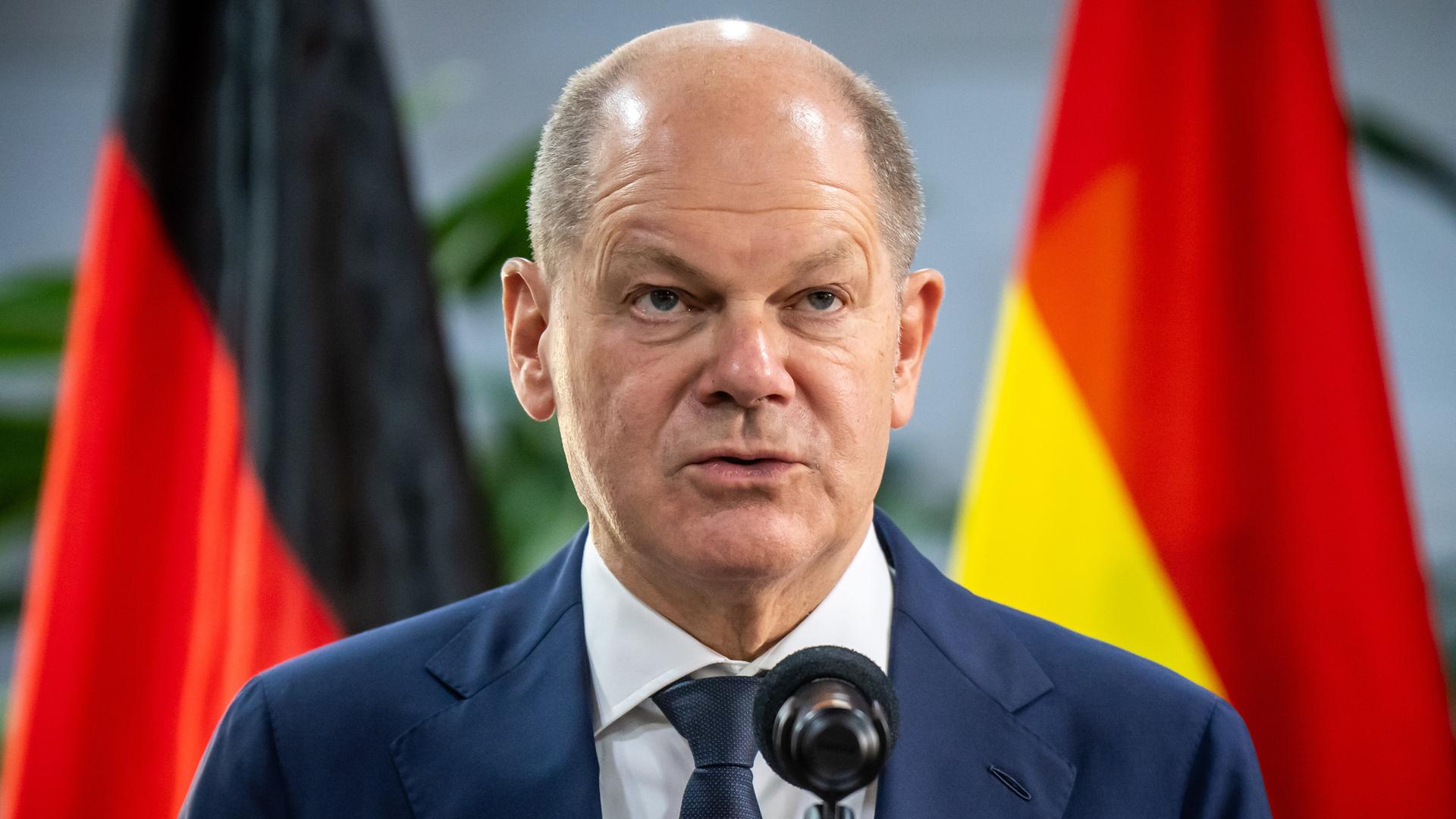 Bundeskanzler Olaf Scholz steht vor einem Mikrofon; im Hintergrund sind Fahnen aufgestellt.
