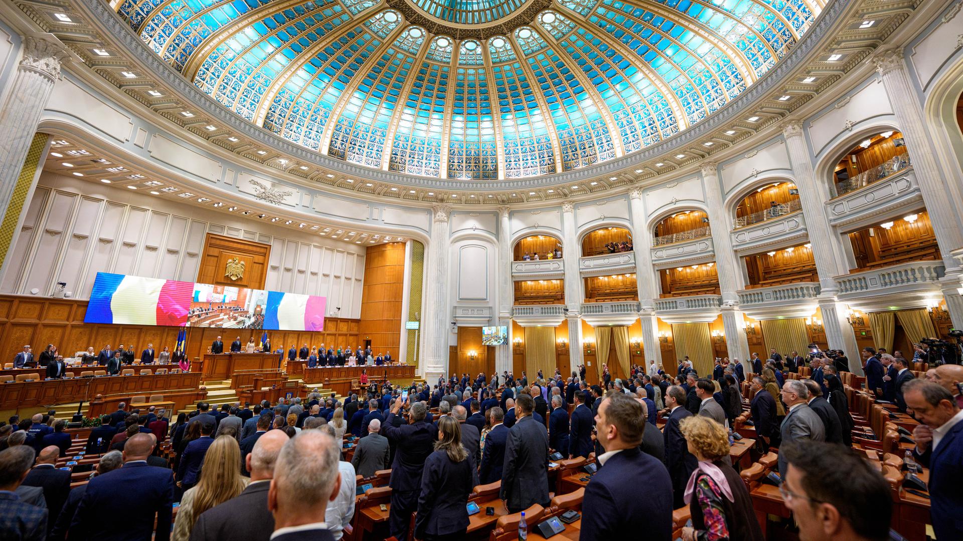 Blick in das vollbesetzte rumänische Parlament in Bukarest mit einer blauen Glaskuppel im Art-Deco-Stil. Die Abgeordneten stehen. Blick in das vollbesetzte rumänische Parlament in Bukarest mit einer blauen Glaskuppel im Art-Deco-Stil. Die Abgeordneten stehen.