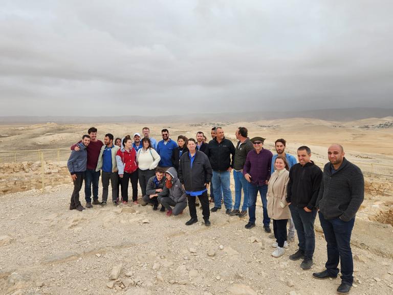 Ein gutes Dutzend Menschen lacht in die Kamera. Hinter ihnen breitet sich die hügelige Negevwüste aus: mit ihren braunen Steinen und unendlichen Mengen von Sand. Ein gutes Dutzend Menschen lacht in die Kamera. Hinter ihnen breitet sich die hügelige Negevwüste aus: mit ihren braunen Steinen und unendlichen Mengen von Sand.