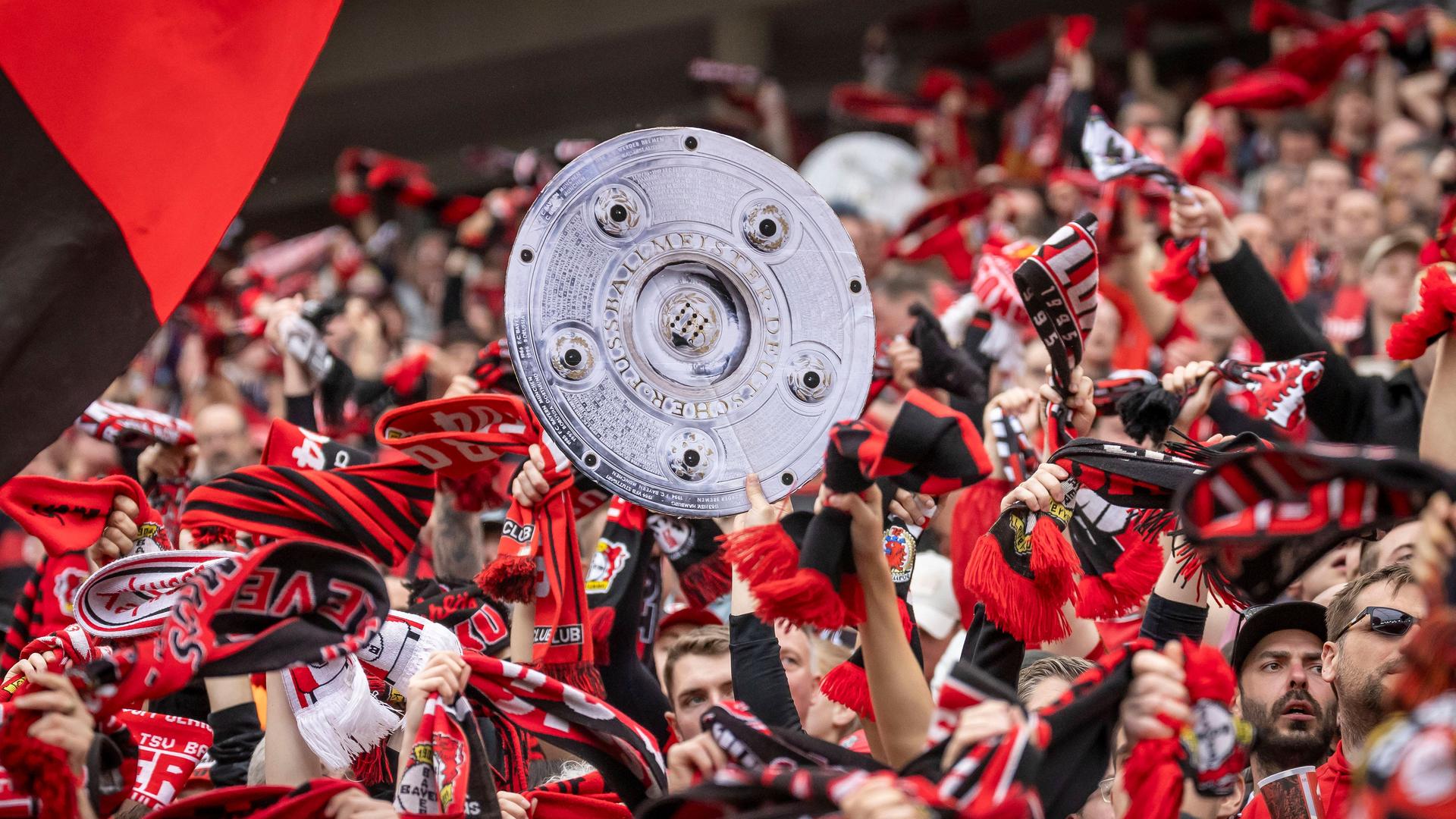 Leverkusen-Fans feiern den Sieg ihrer Mannschaft und halten eine Kopie der Meisterschale in die Höhe.
