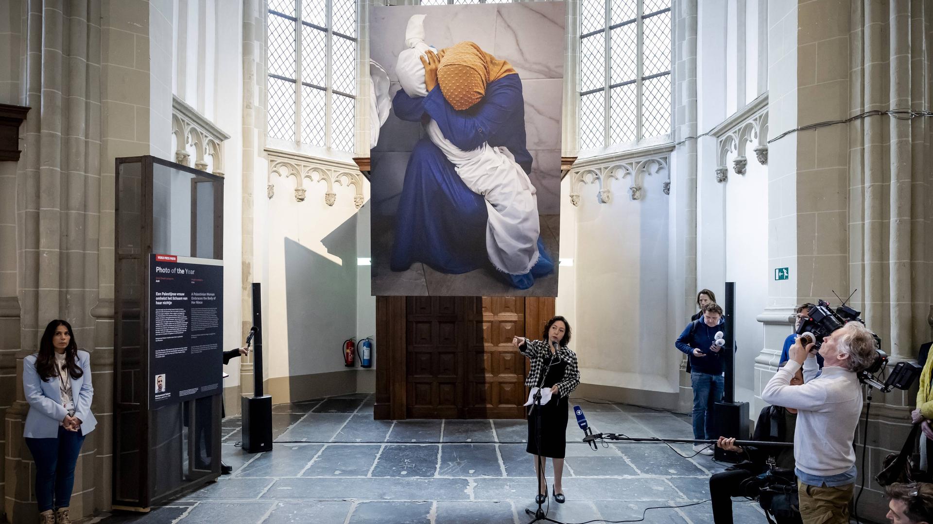 In der Nieuwe Kerk in Amsterdam werden die Sieger des "World Press Photo Awards" verkündet. Das Siegerbild hängt in riesiger Version unter der Decke. Es zeigt Ina Abu Maamar, die ein blaues Kleid und ein ockerfarbenes Kopftuch trägt. Sie beugt sich über den in ein weißes Laken gehüllten Leichnam ihrer fünf Jahre alten Nichte Saly.