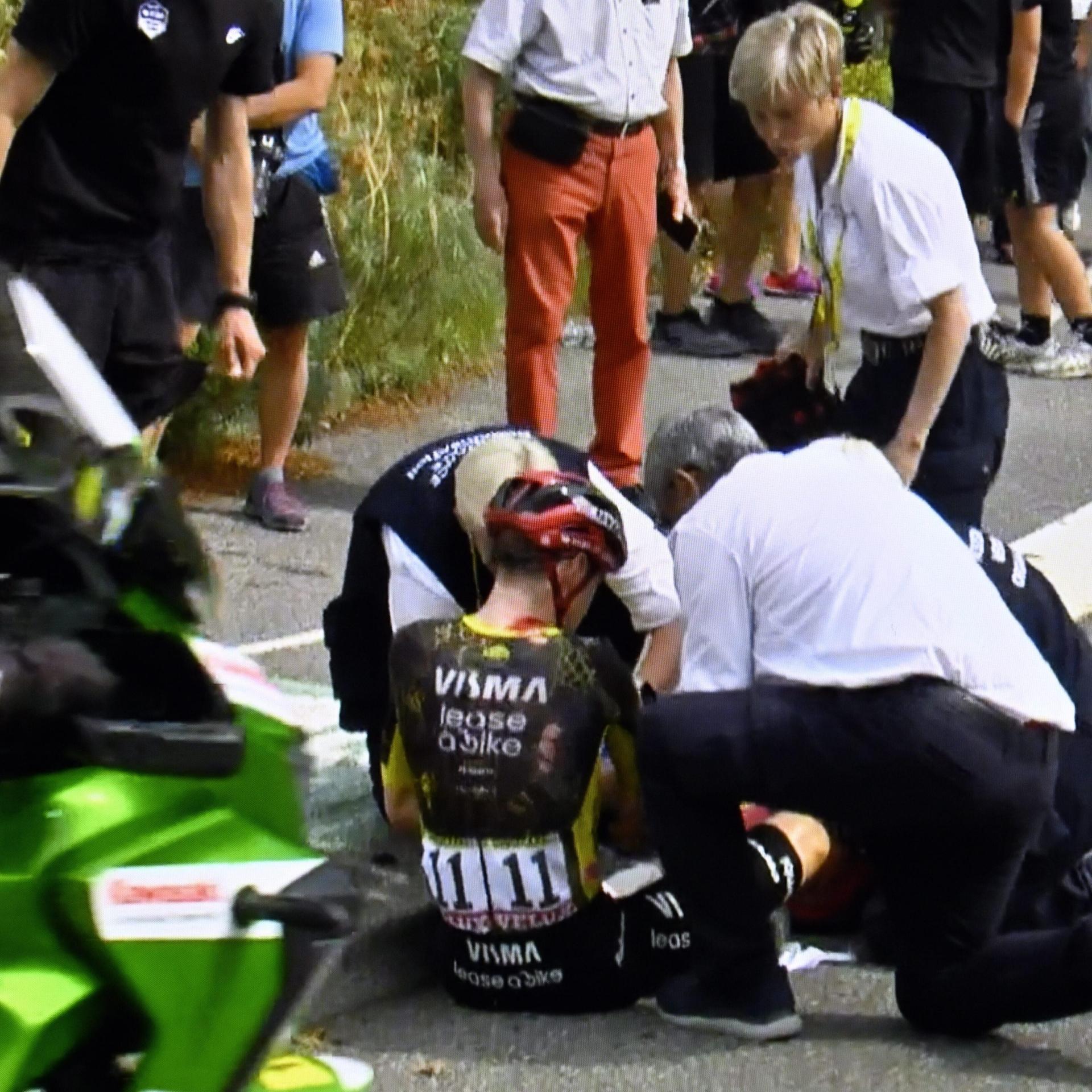 Zwei Männer kümmern sich um Jonas Vingegaard, der nach einem Sturz bei der Tour de France verletzt auf der Straße sitzt.