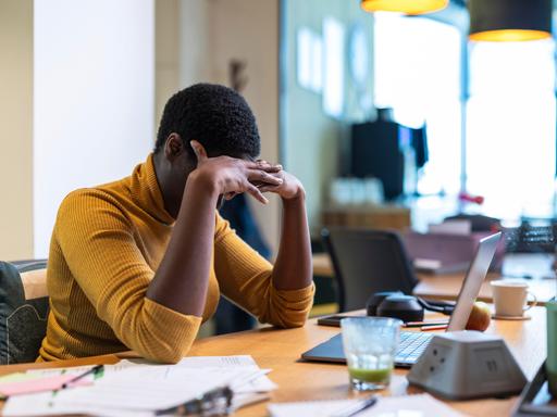 Eine Frau sitzt an einem Schreibtisch und hält sich die Hände vors Gesicht