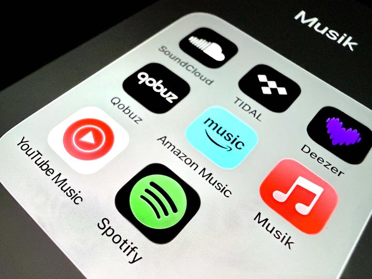 Auf einem Handydisplay sind Apps verschiedener Musikstreamingplattformen zu sehen.