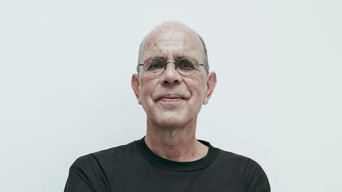 Ein Mann mit schwarzem Shirt und Brille verschränkt die Hände unter den Achseln udn schaut direkt in die Kamera