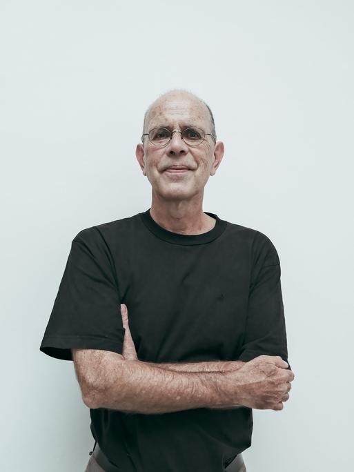 Ein Mann mit schwarzem Shirt und Brille verschränkt die Hände unter den Achseln udn schaut direkt in die Kamera