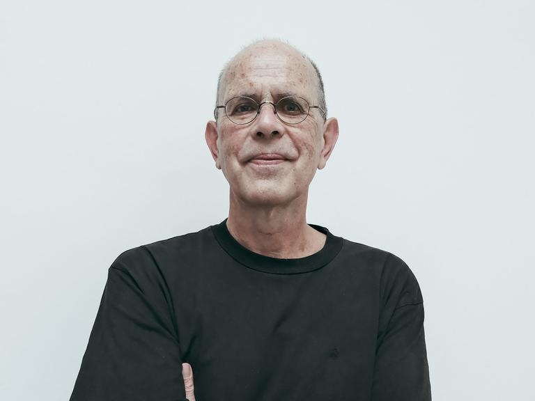 Ein Mann mit schwarzem Shirt und Brille verschränkt die Hände unter den Achseln udn schaut direkt in die Kamera