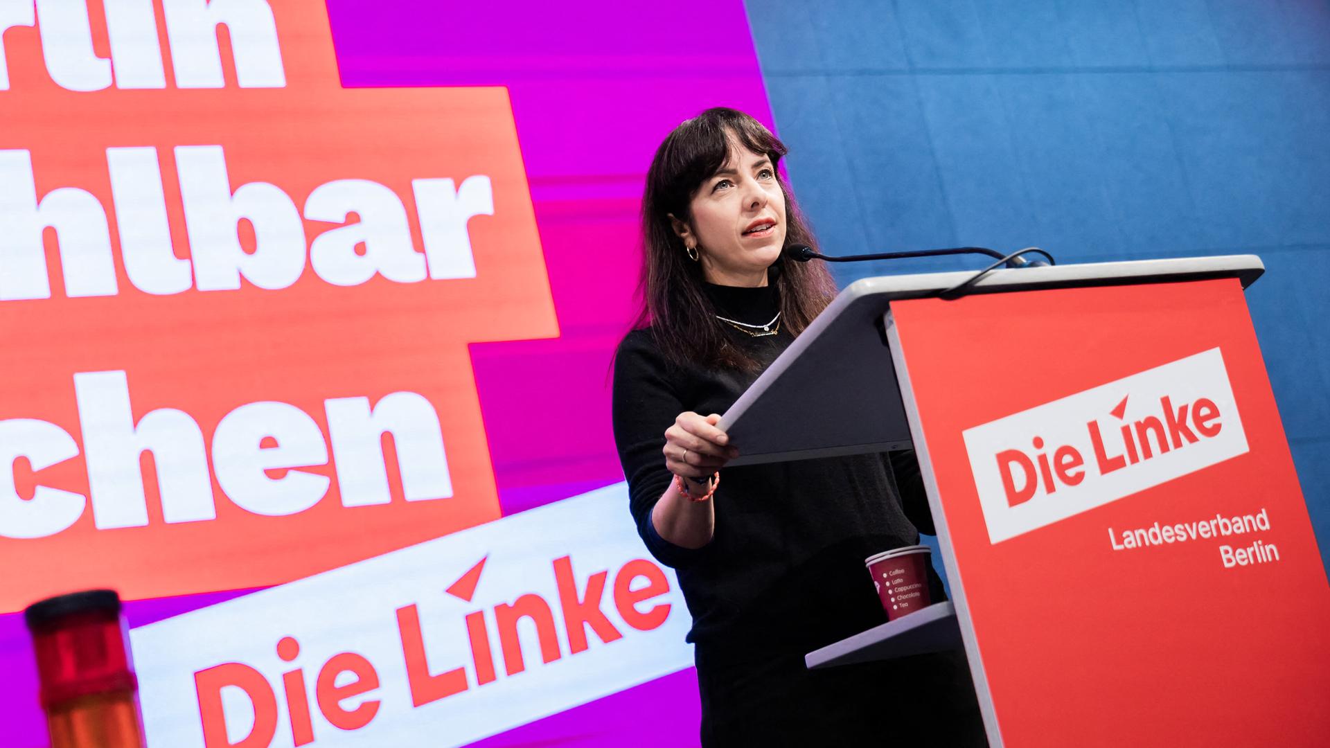 Eralp steht an einem Redpult. Im Hintergrund ist ein Schriftzug der Linkspartei zu sehen.