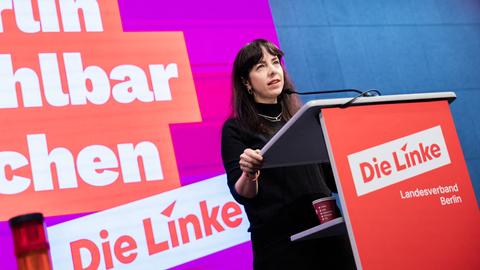 Eralp steht an einem Redpult. Im Hintergrund ist ein Schriftzug der Linkspartei zu sehen.