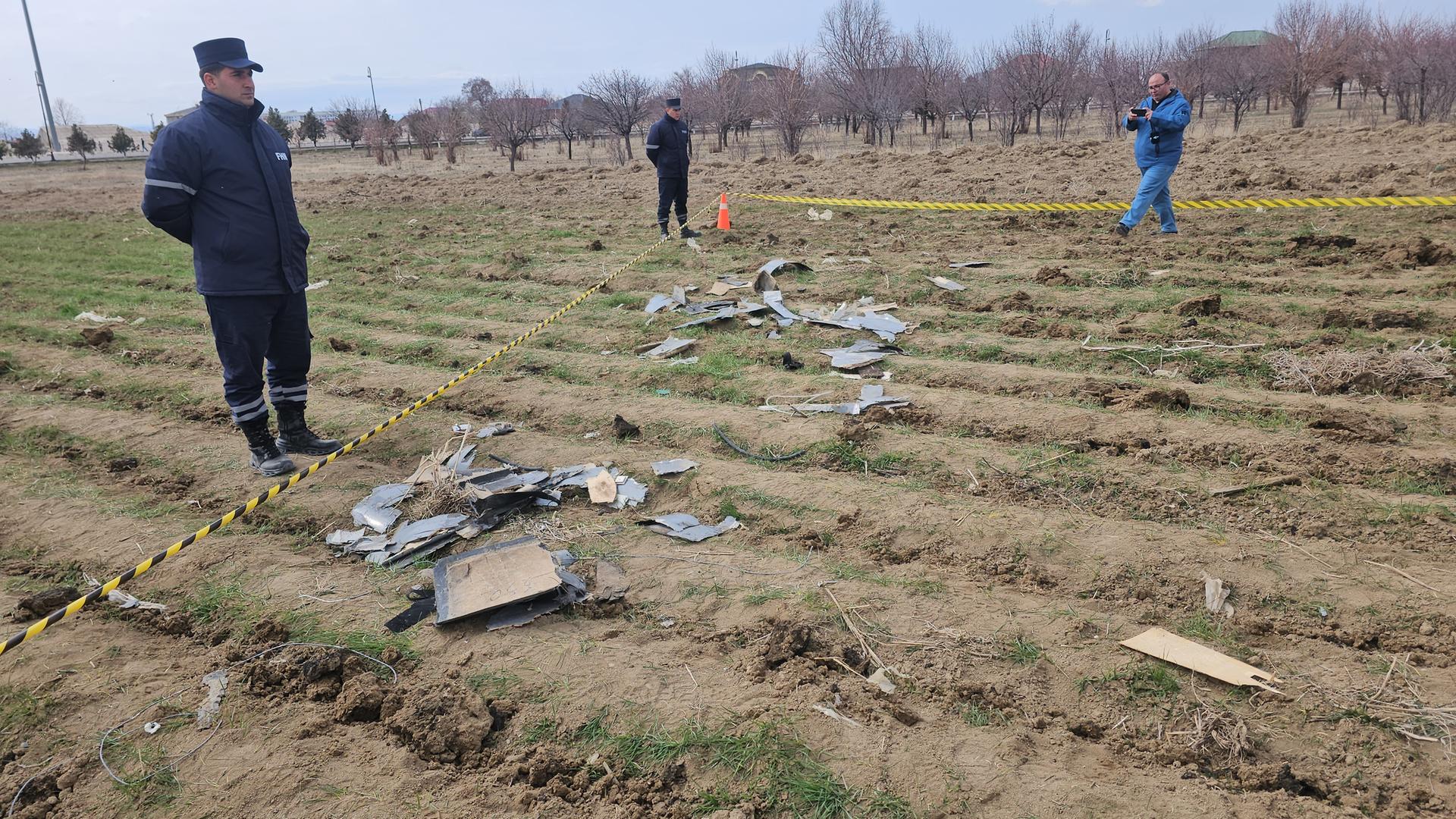 Auf einem Feld liegen Trümmerteile einer Drohne. Der Bereich ist mit gelb-schwarzem Plastikband abgesperrt. Dahinter stehen Polizisten.