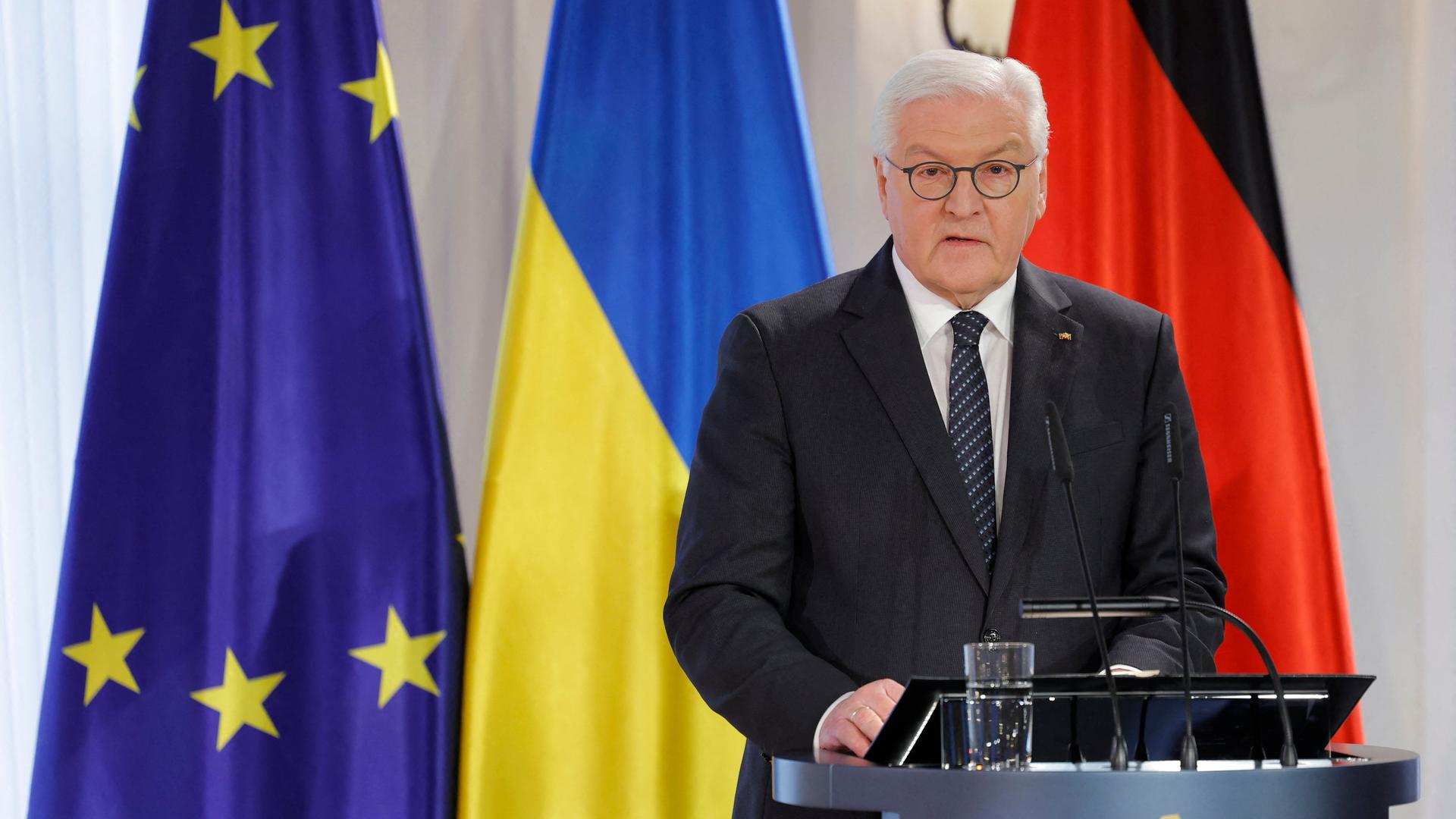 Bundespräsident Steinmeier steht an einem Redepult. Er trägt einen schwarzen Anzug und eine schwarze Krawatte. Im Hintergrund sieht man die ukrainische und die deutsche Flagge sowie die Flagge der EU.