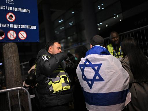 Israelische Fans kommen zum Spiel Frankreich gegen Israel und unterhalten sich mit der Polizei. Ein Fan hat eine Israel-Flagge um den Körper. 