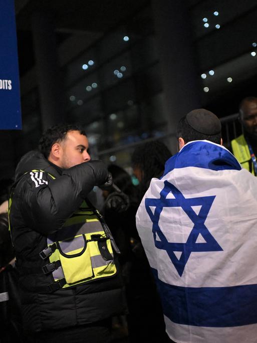 Israelische Fans kommen zum Spiel Frankreich gegen Israel und unterhalten sich mit der Polizei. Ein Fan hat eine Israel-Flagge um den Körper. 