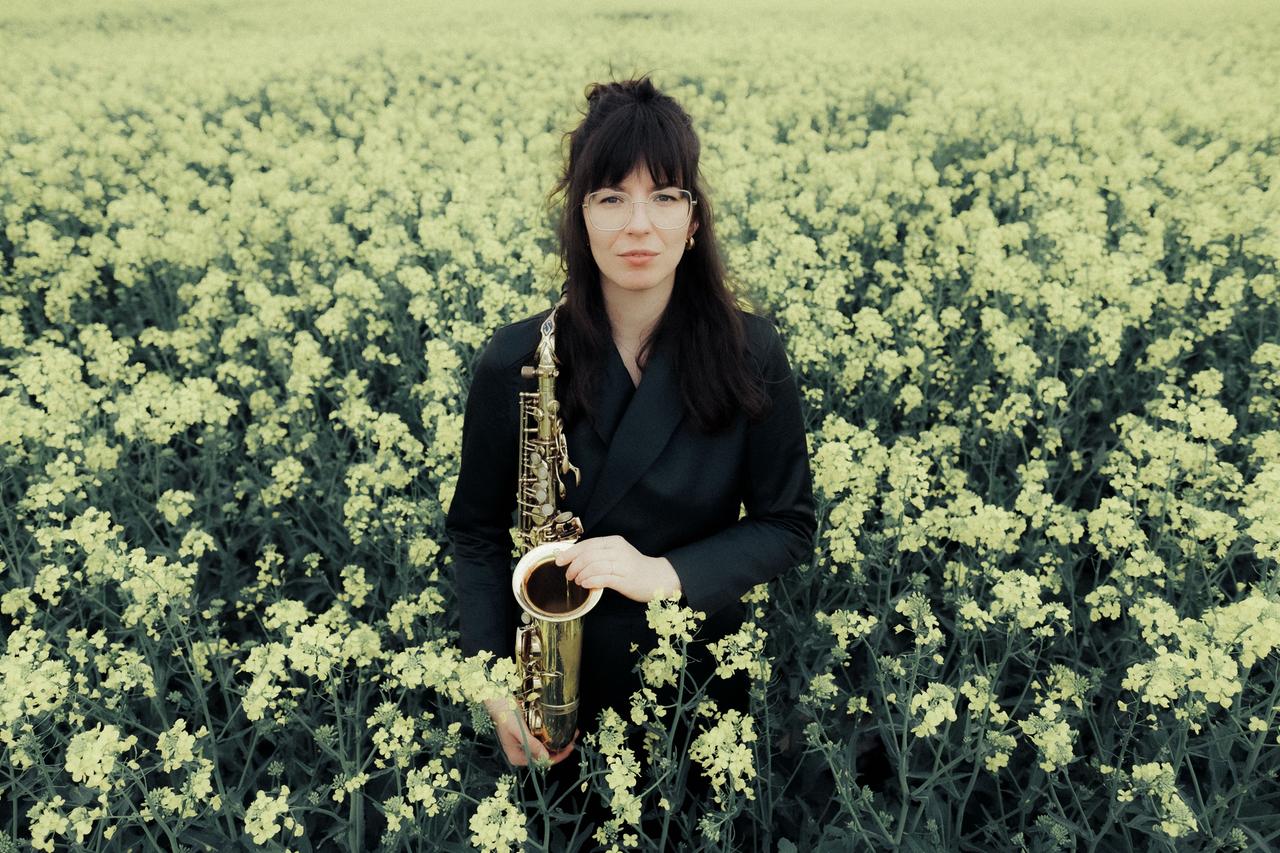Die Saxophonistin mit langen dunklen Haaren steht mit ihrem Instrument in einem blühenden Rapsfeld. Die Saxophonistin mit langen dunklen Haaren steht mit ihrem Instrument in einem blühenden Rapsfeld.