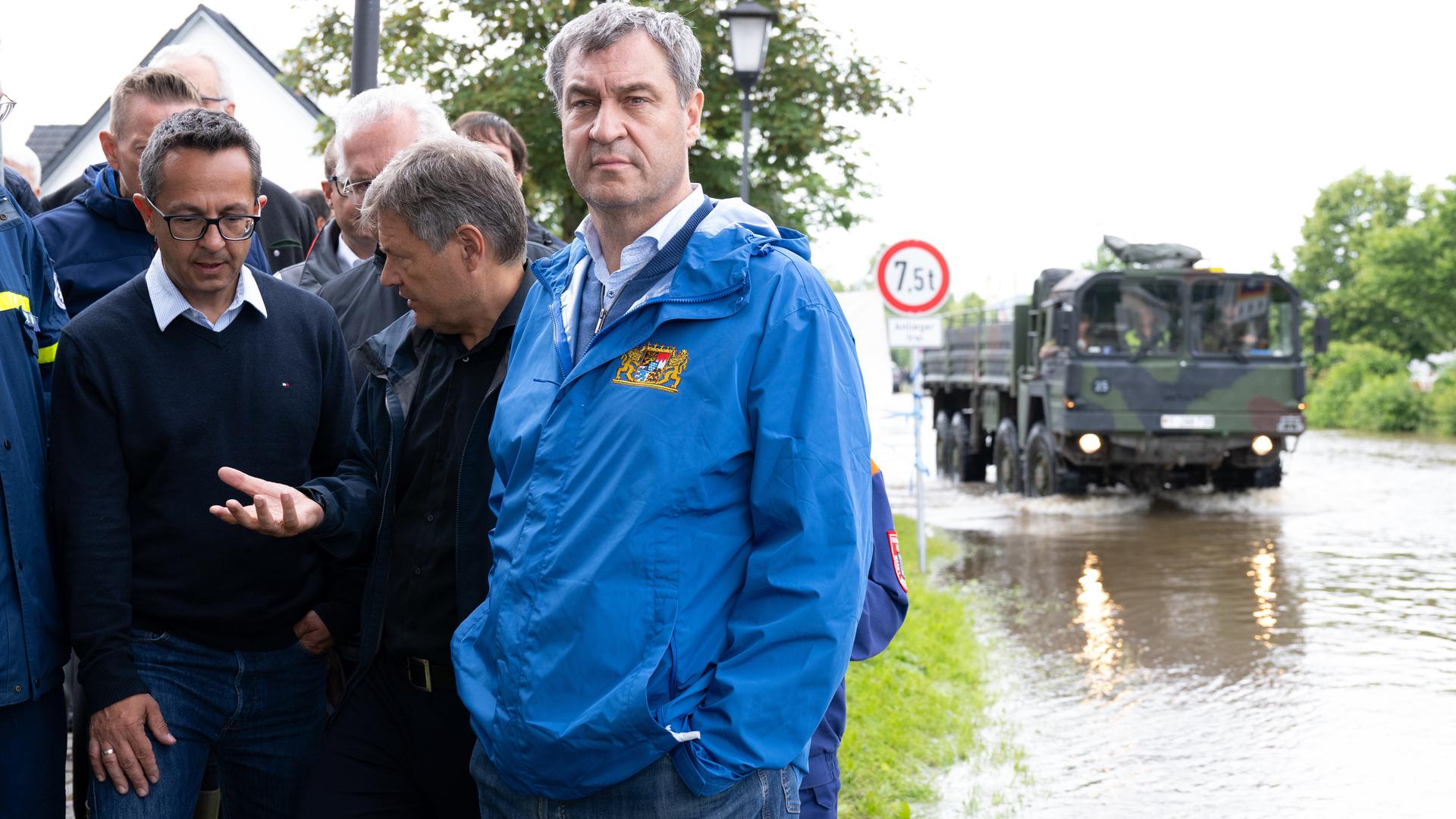 Bayerns Ministerpräsident Markus Söder (CSU), Bundeswirtschaftsminister Robert Habeck (Bündnis/90 Die Grünen), und der Bürgermeister von Reichertshofen, Michael Franken, stehen am Rande einer überfluteten Straße.