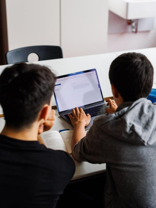 Schüler eines Gymnasiums sitzen vor einem Laptop und benutzen ein KI-Tool. Sie sind von hinten zu sehen und blicken auf ihre Laptops. 