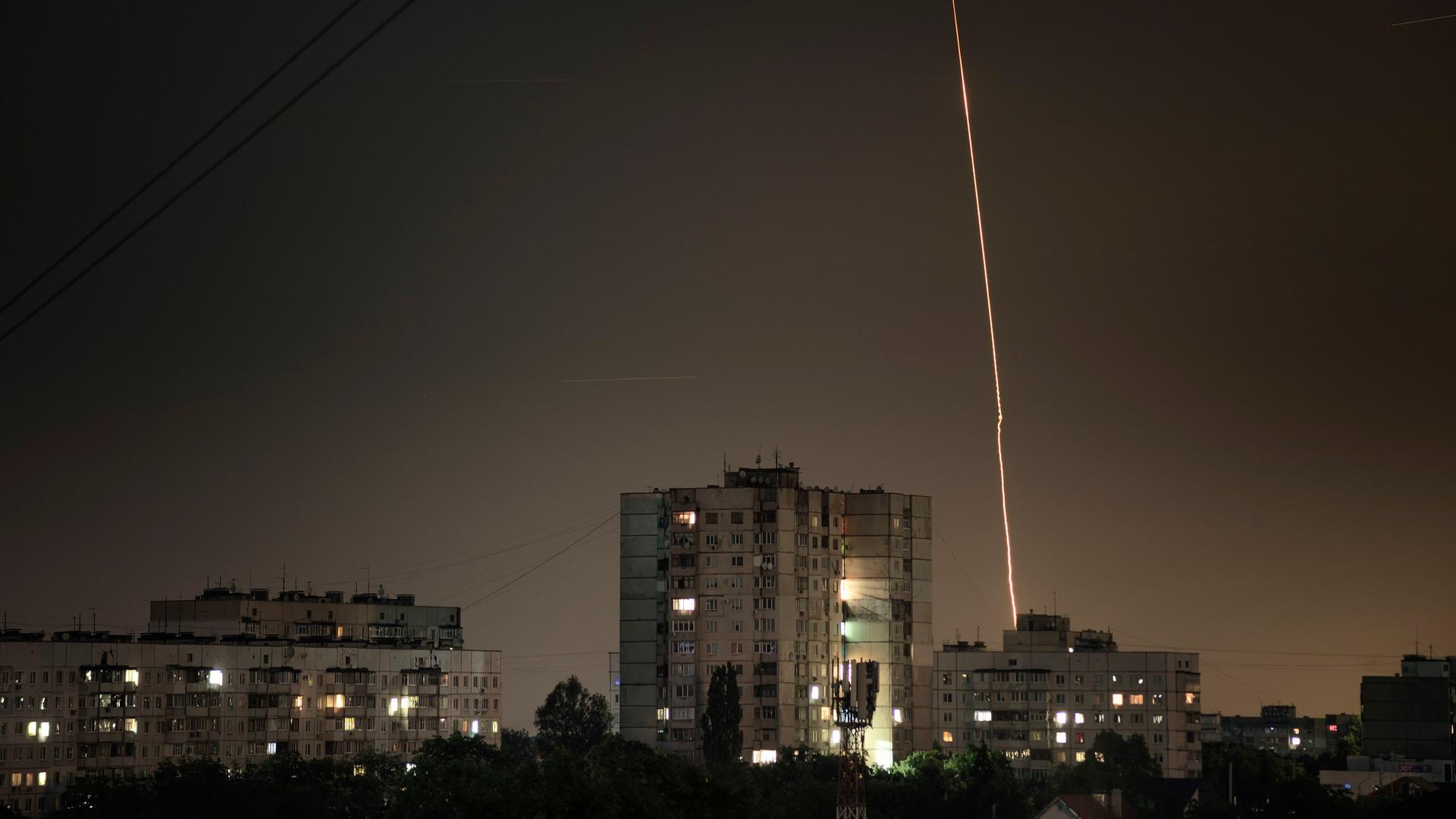 Man sieht ein Stadtviertel in der Nacht. Ein heller Streifen vom Himmel zur Erde zeigt entweder eine einschlagende Rakete oder eine aufsteigende Abwehrrakete.