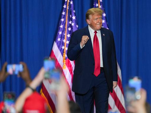 Donald Trump auf einer Wahlkampfveranstaltung im US-Bundesstaat North Carolina. Im Hintergrund ist die US-Flagge zu sehen. Im Vordergrund halten viele Zuschauer ihre Smartphones zum Fotografieren hoch.