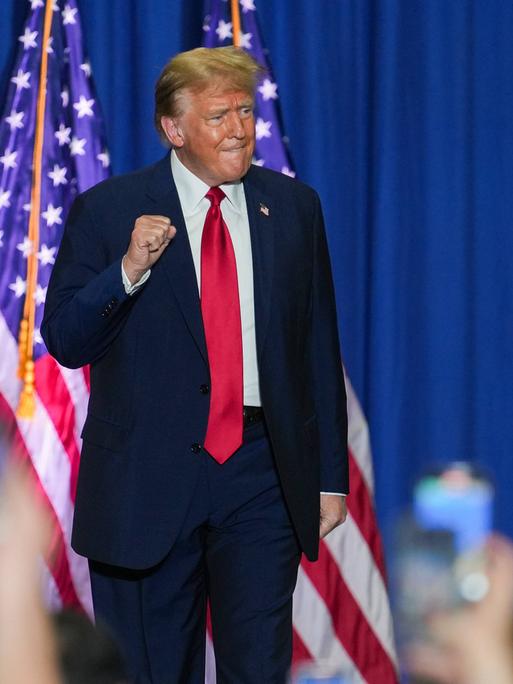 Donald Trump auf einer Wahlkampfveranstaltung im US-Bundesstaat North Carolina. Im Hintergrund ist die US-Flagge zu sehen. Im Vordergrund halten viele Zuschauer ihre Smartphones zum Fotografieren hoch.