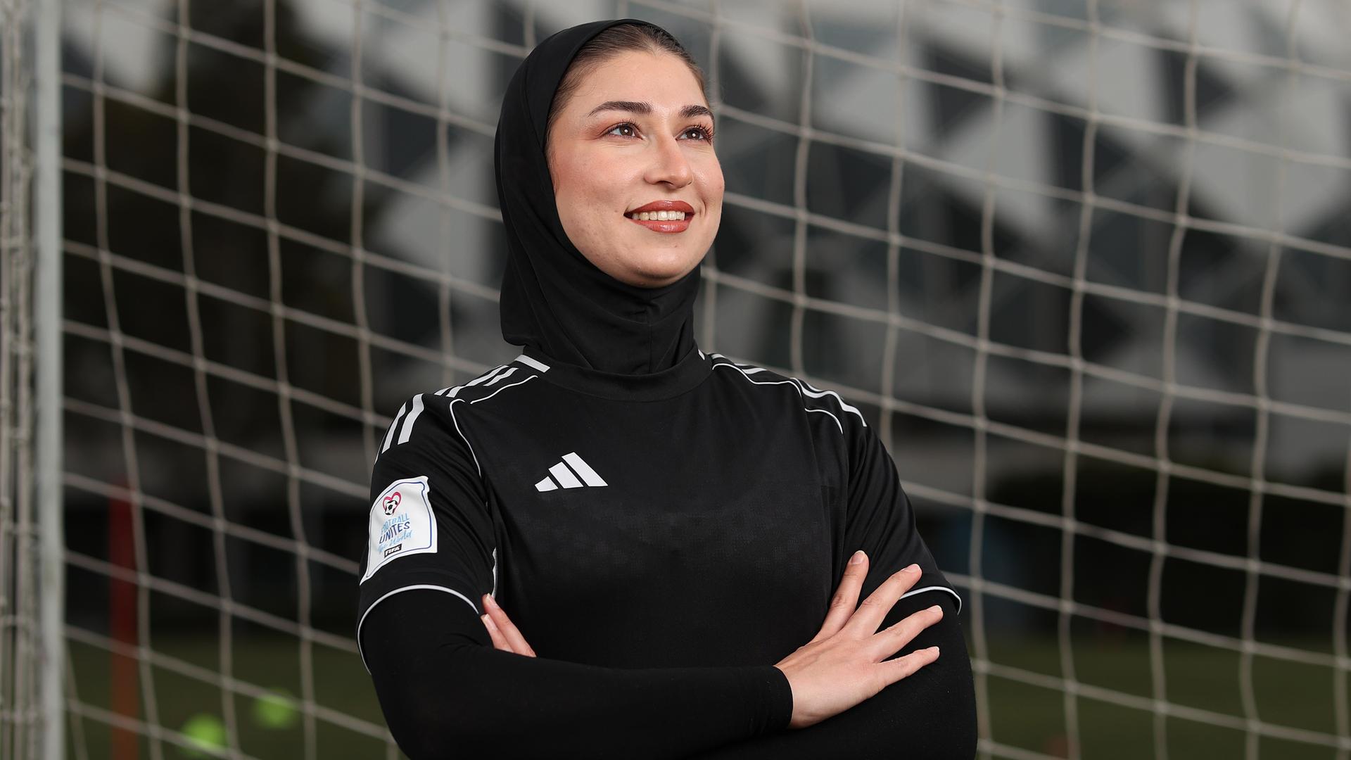 Mursal Sadat von der "Afghan Woman United" Fussballmannschaft posiert vor einem Tornetz. Sie trägt schwarze Spielkleiderung. 
