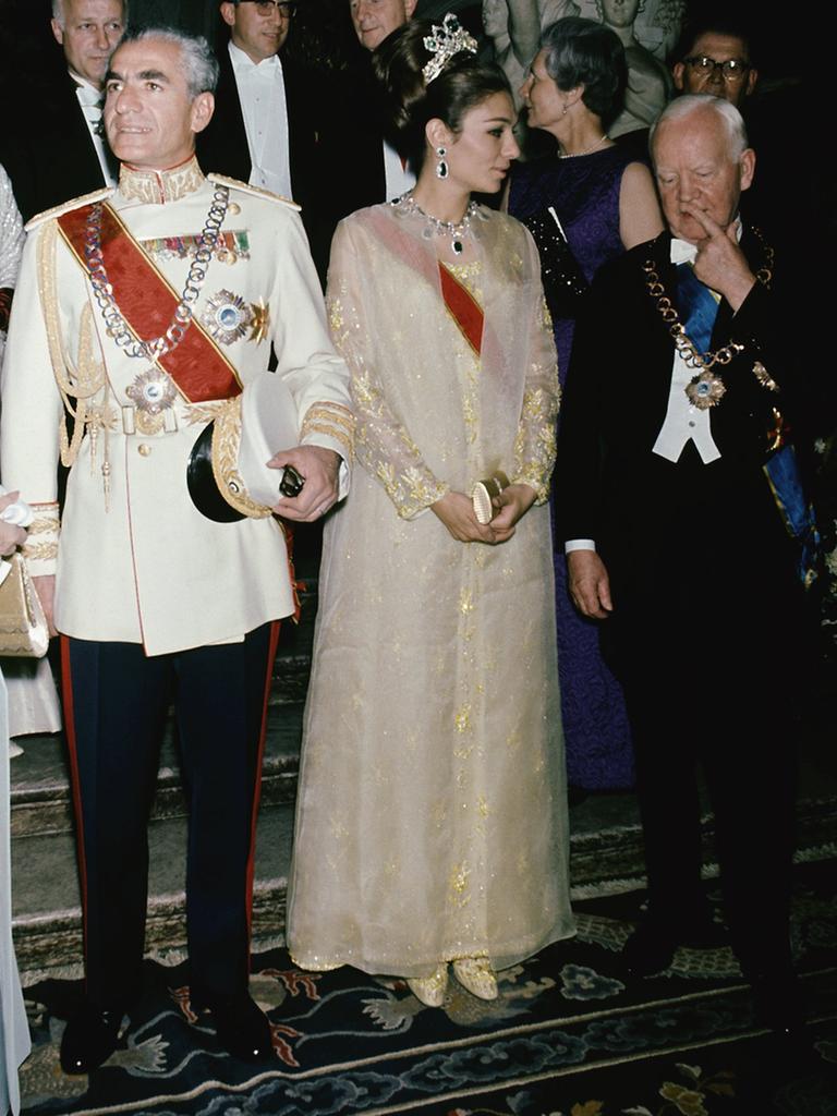 Großer diplomatischer Empfang. Eine ältere Frau im pelzbesetzten Kleid, ein älterer Herr in Uniform, eine jüngere Frau mit einem Krönchen im Haar und ein älterer Herr im Anzug stehen auf einem Teppich.