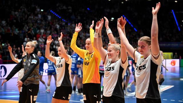 Mehrere Handballerinnen halten ihre Hände hoch und lächeln nach ihrem Sieg. 