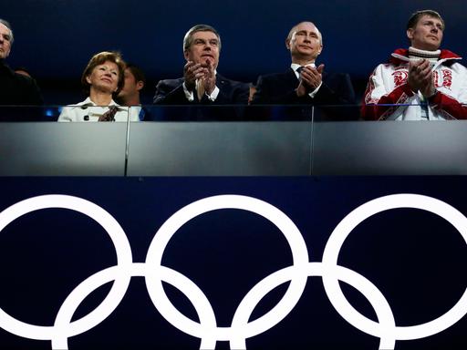 Russlands Präsident Vladimir Putin und IOC-Präsident Thomas Bach stehen gemeinsam bei der Abschlussfeier in Sotchi 2014, unter sich die Olympische Ringe.