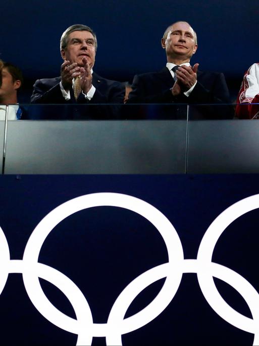 Russlands Präsident Vladimir Putin und IOC-Präsident Thomas Bach stehen gemeinsam bei der Abschlussfeier in Sotchi 2014, unter sich die Olympische Ringe.