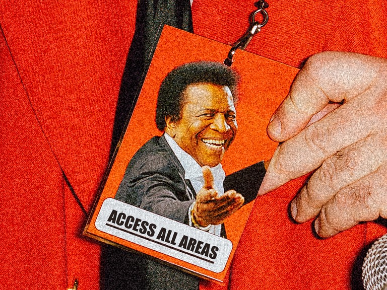 Die Grafik zeigt ein Bild von Roberto Blanco auf einer Akkrediterungskarte, die Zugang zu allen Bereichen gewährt. Diese wird von jemandem getragen und vorgezeigt, der ein rotes Jacket trägt - das Gesicht desjenigen sieht man nicht. 
