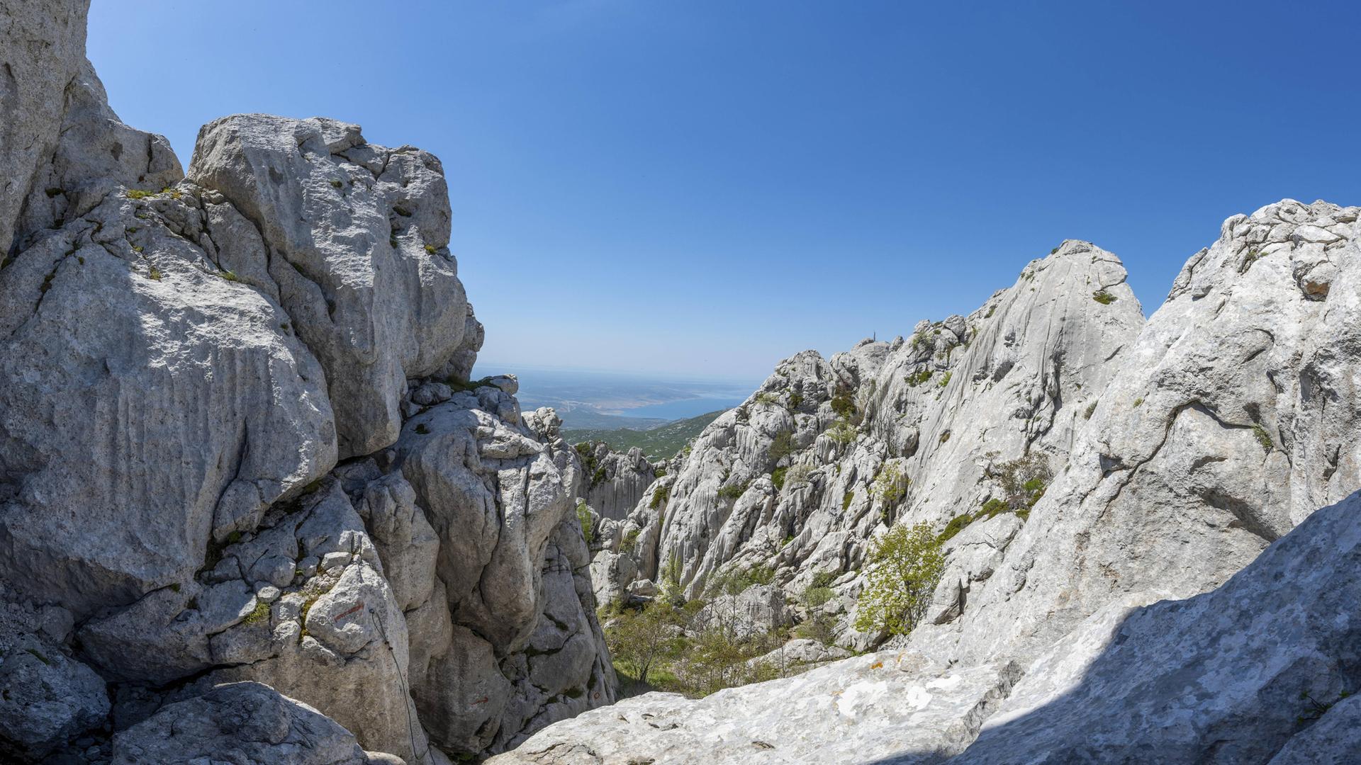 Im Vordergrund eine schroffe Gebirgslandschaft, im Hintergrund das Meer.