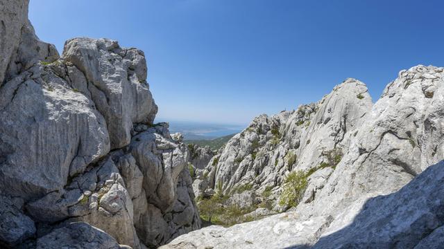 Im Vordergrund eine schroffe Gebirgslandschaft, im Hintergrund das Meer.