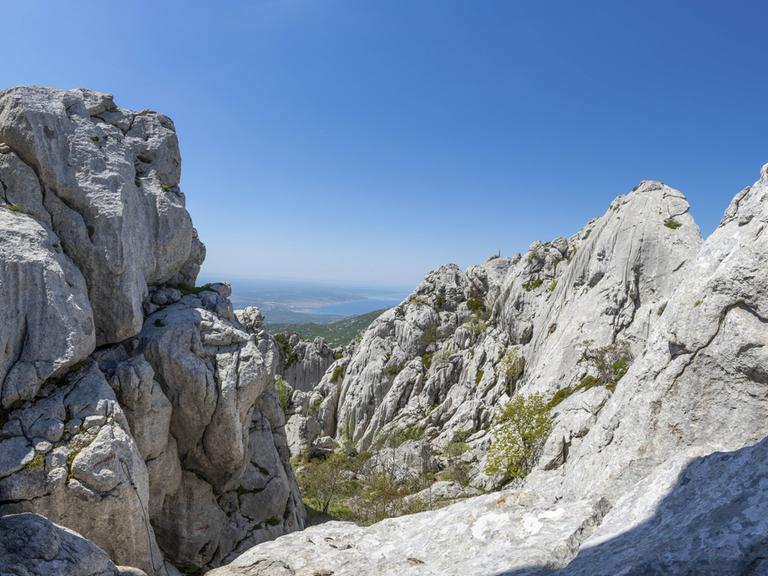 Im Vordergrund eine schroffe Gebirgslandschaft, im Hintergrund das Meer.