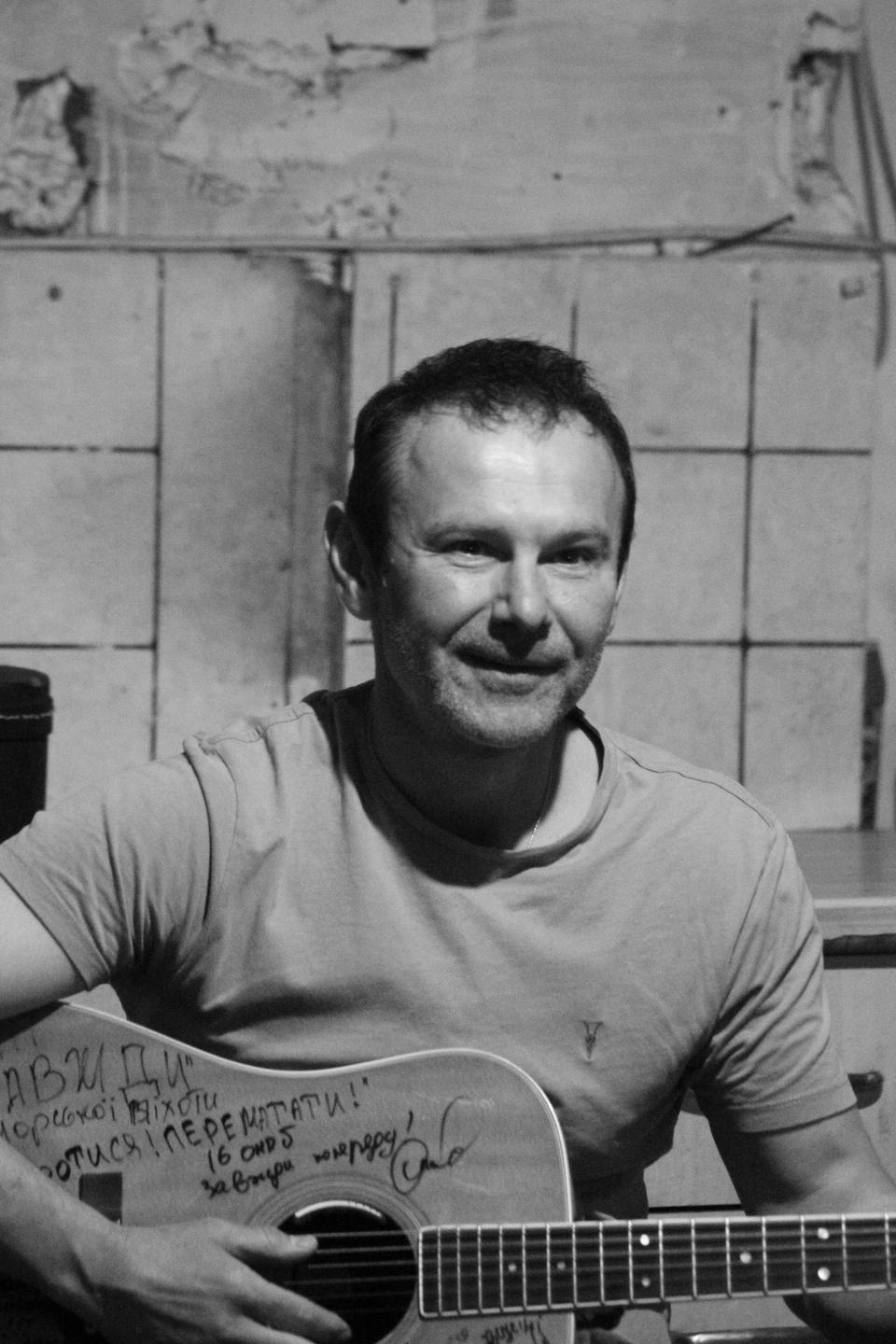 Der Sänger Warkatschuk hält eine Gitarre in der Hand, auf die ukrainische Einheiten Grüße geschrieben haben.