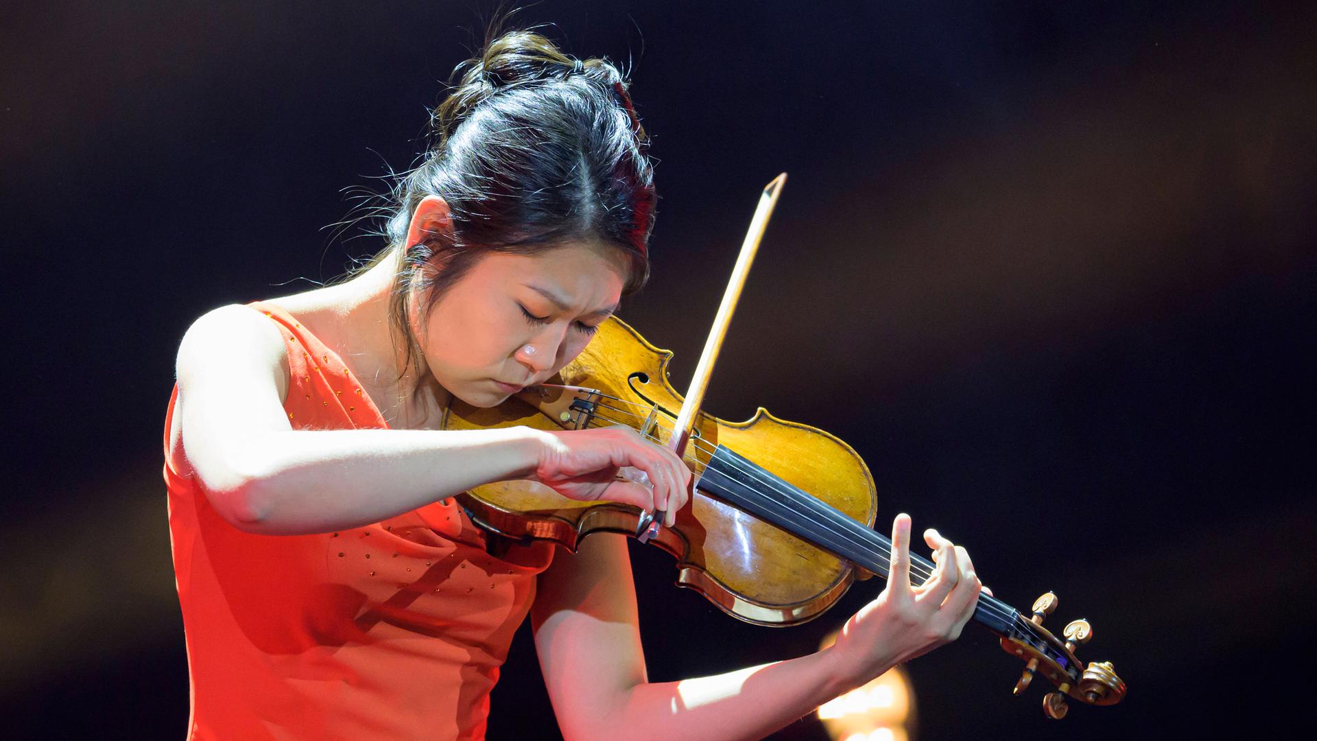Tianwa YANG steht in einem roten Kleid uns spielt auf ihrer scheinbar goldenen Geige.