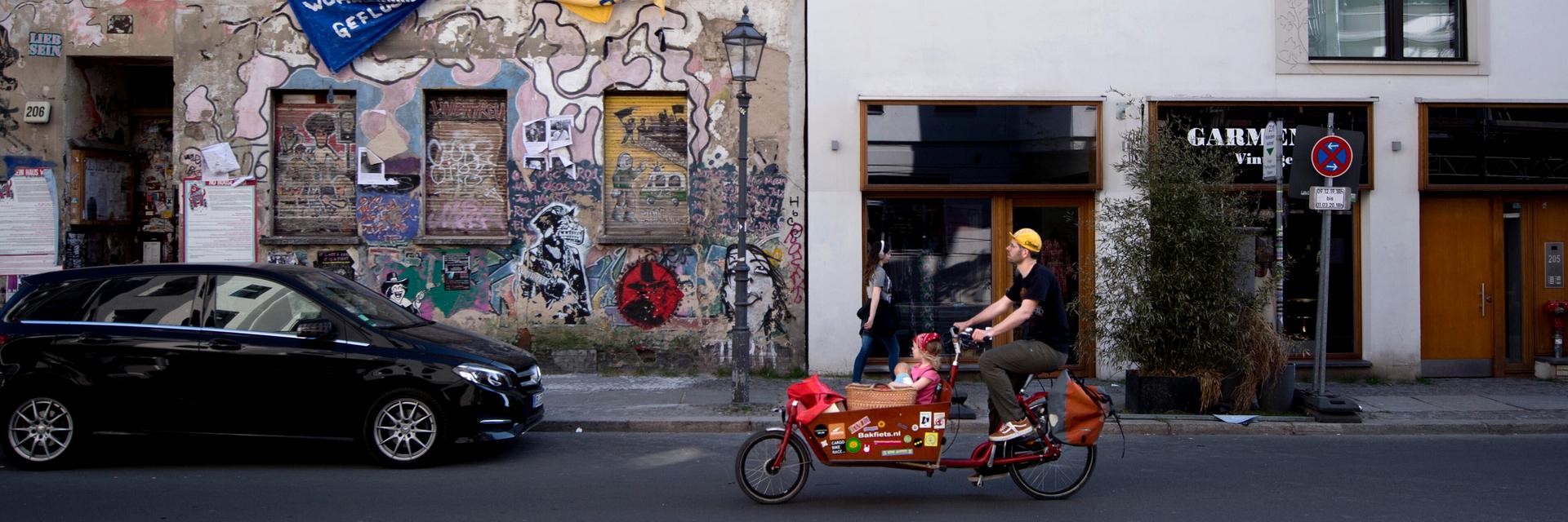 Ein Fahrradfahrer fährt an einem Neubau neben einem Besetztes Haus in Berlin Mitte vorbei. 