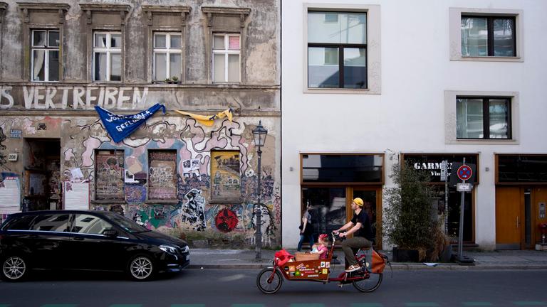 Ein Fahrradfahrer fährt an einem Neubau neben einem Besetztes Haus in Berlin Mitte vorbei. 