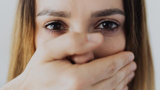 Eine Frau, der eine Hand vor den Mund gehalten wird.