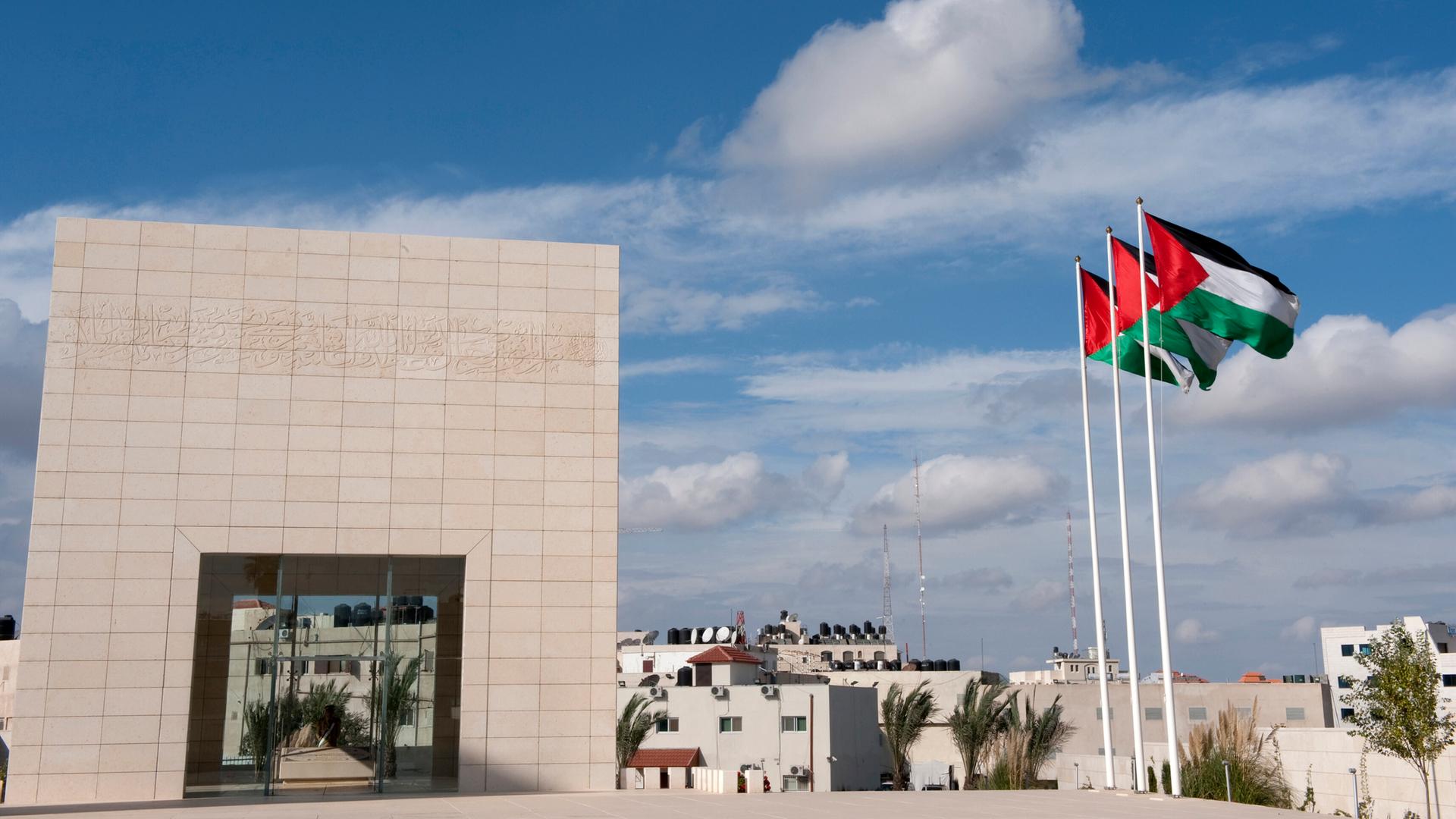 Ein viereckiges Gebäude nehmen Fahnenmasten mit palästinensischen Flaggen