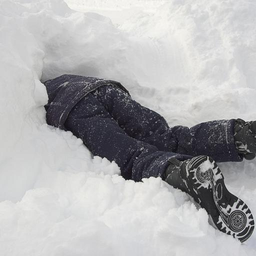Ein Kind in dunkler Winterkleidung steckt Kopf voran in einem Schneehaufen.