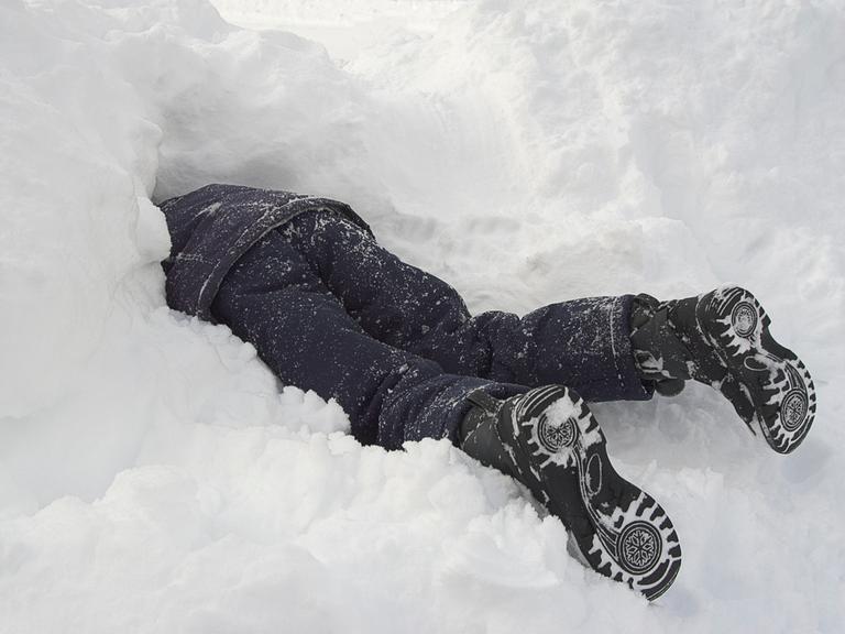 Ein Kind in dunkler Winterkleidung steckt Kopf voran in einem Schneehaufen.