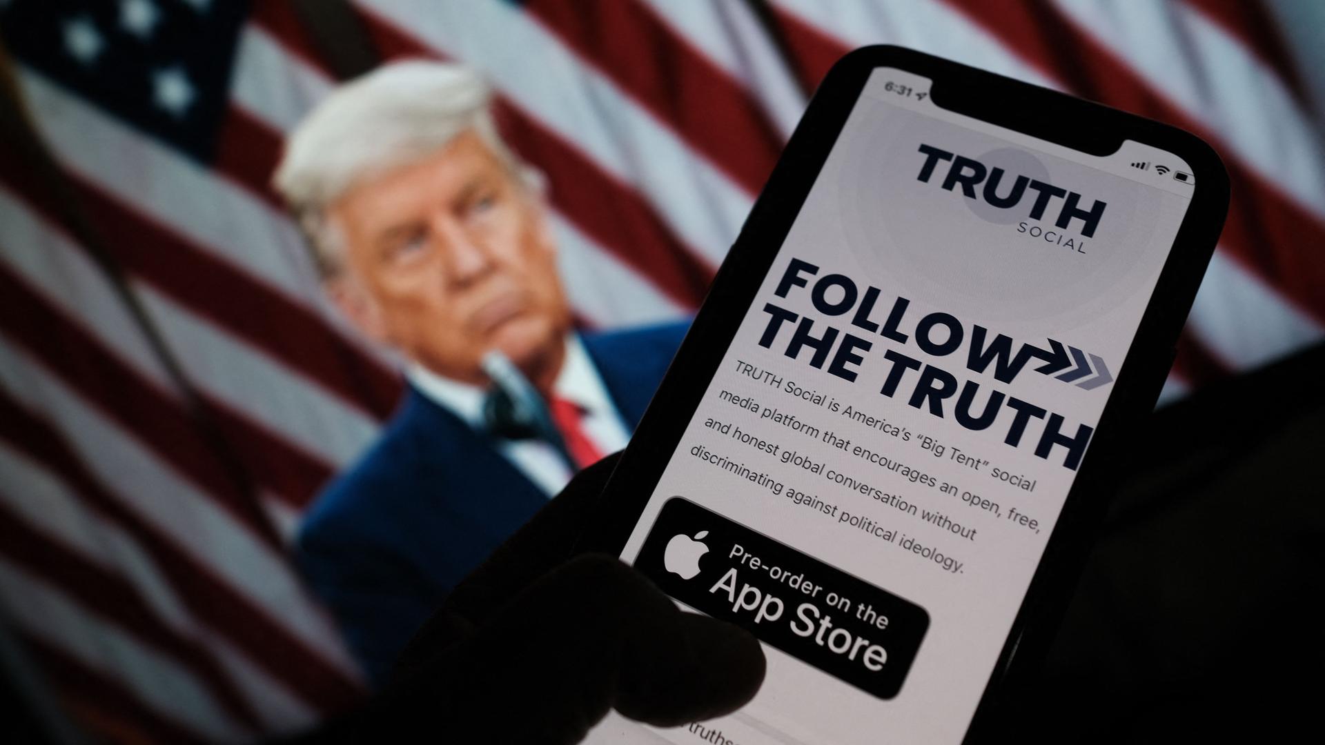 Ein App Store auf einem Handy, auf dem man "Truth Social" herunterladen kann. Im Hintergrund Donald Trump als Screen.