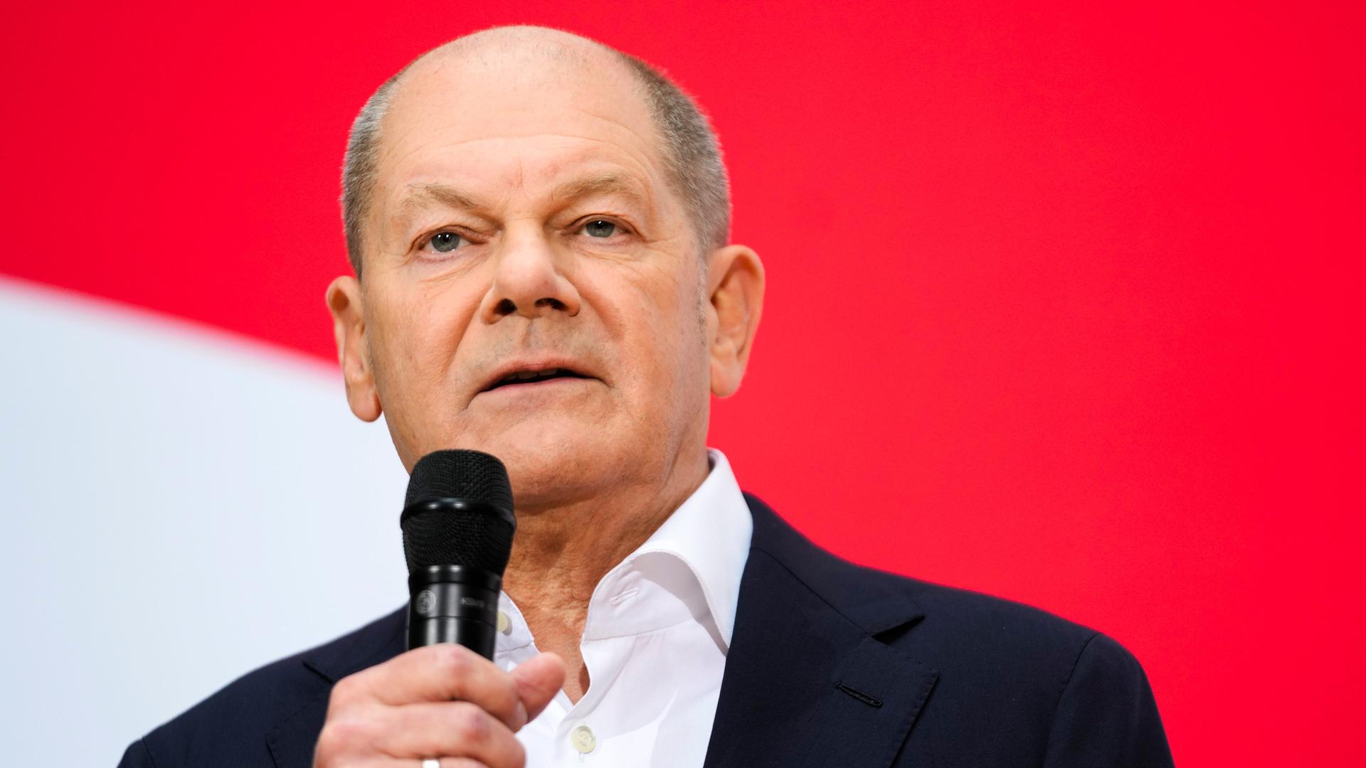 Bundeskanzler Olaf Scholz (SPD) spricht auf einer Pressekonferenz und hält ein Mikrofon in der Hand.