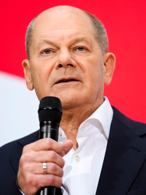 Bundeskanzler Olaf Scholz (SPD) spricht auf einer Pressekonferenz und hält ein Mikrofon in der Hand.