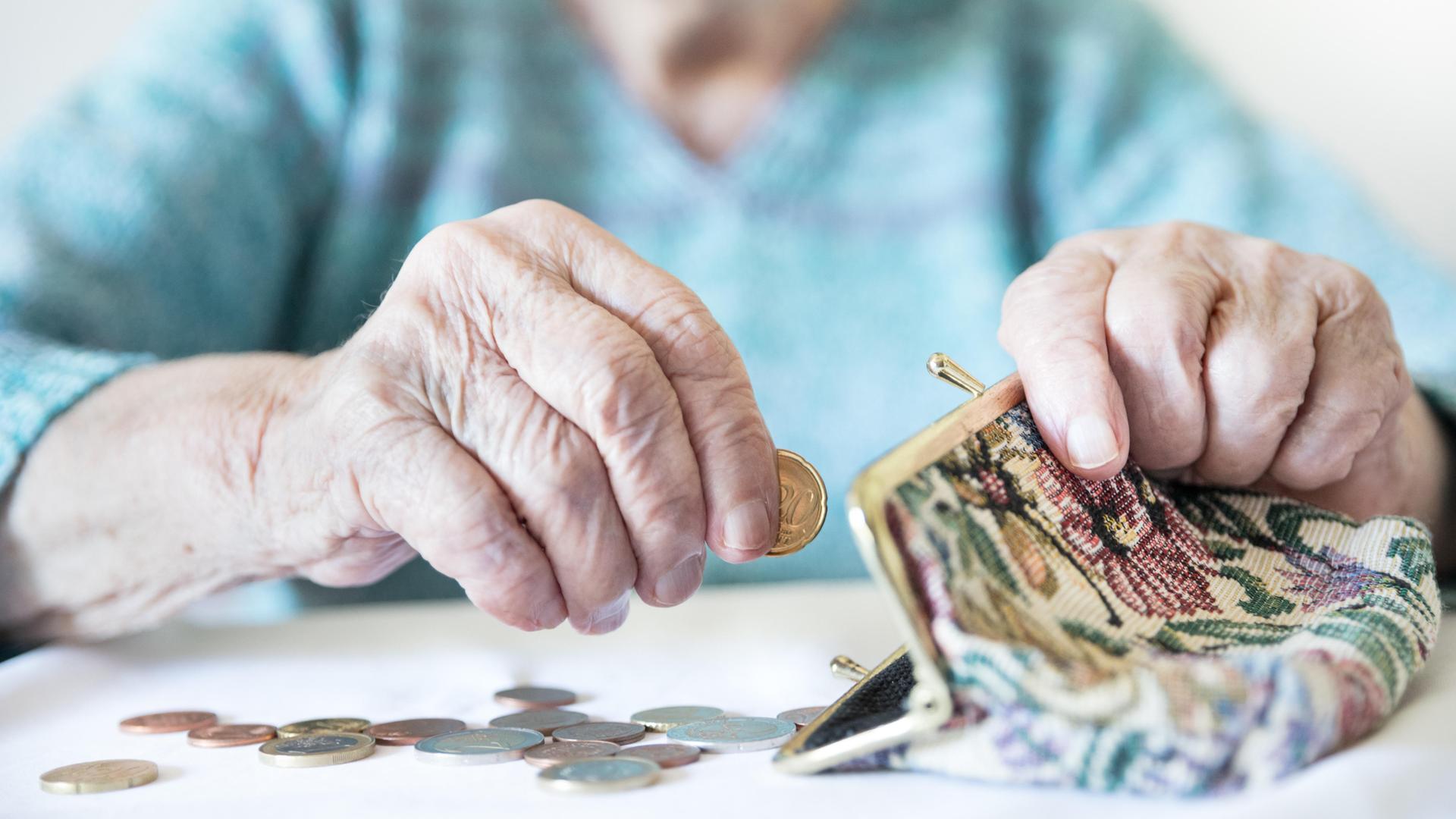 Eine alte Frau zählt ihr Geld und hat eine Geldbörse vor sich liegen.  