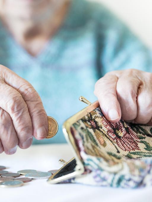 Eine alte Frau zählt ihr Geld und hat eine Geldbörse vor sich liegen.  