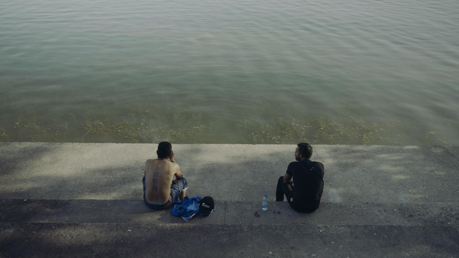 Zwei Männer sitzen auf einer Stufe am Wasser.