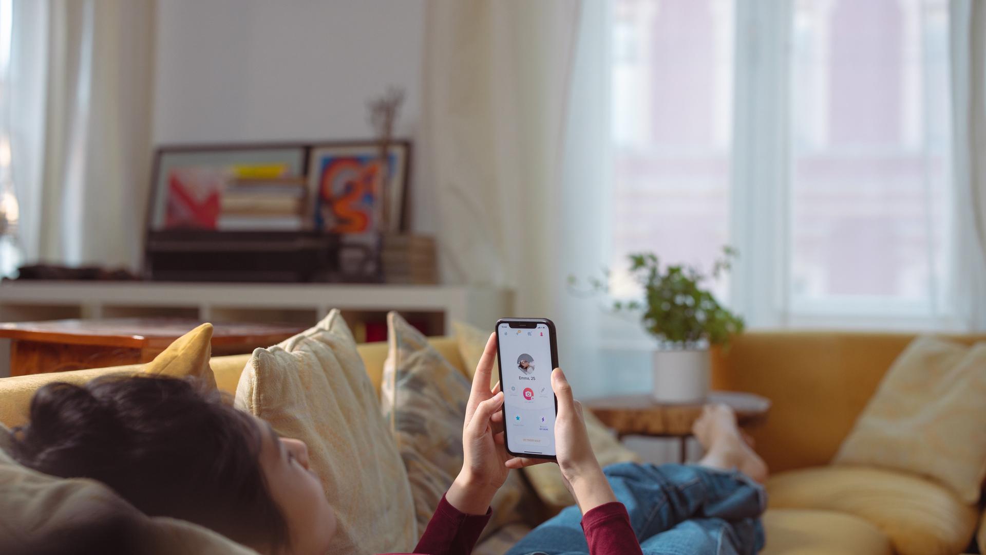 Eine Frau liegt auf dem Sofa und hat auf dem Smartphone eine Dating-App geöffnte
