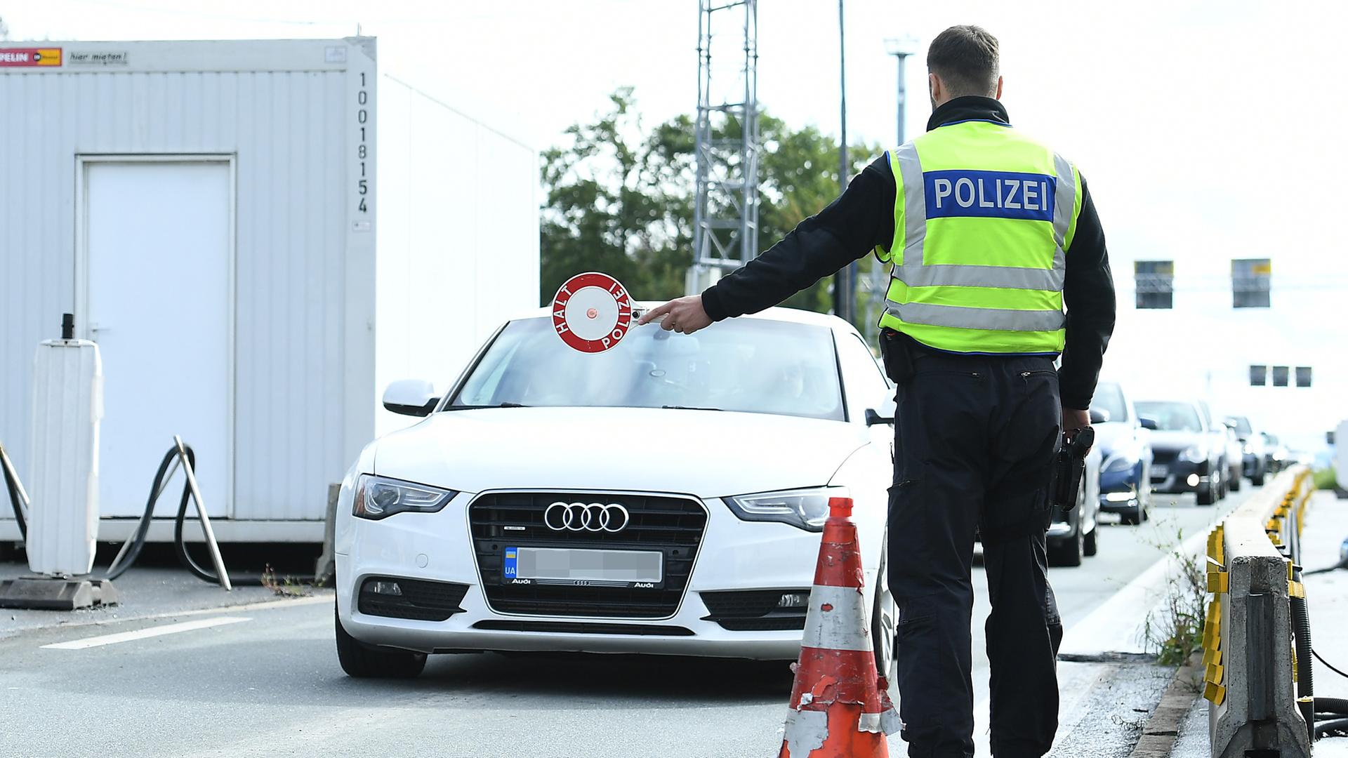 Die Bundes-Regierung hat beschlossen: Die Kontrollen an den Grenzen von Deutschland werden verlängert. Das Foto zeigt einen Polizisten, der eine Kelle hochhält. Er will ein Auto anhalten, das in seine Richtung fährt.