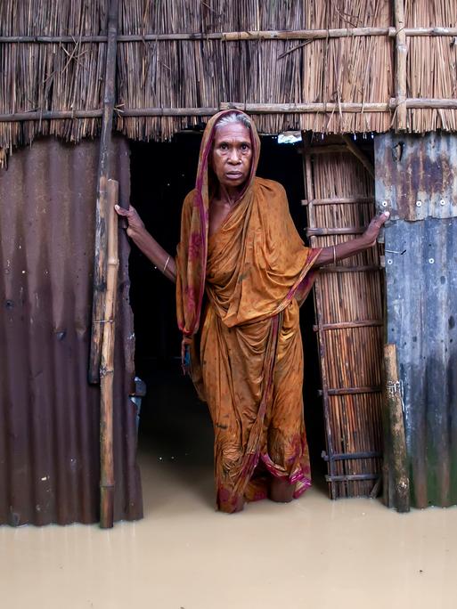 Eine ältere Frau steht am 6. Oktober 2024 vor ihrem Haus im knietiefen Hochwasser in einem Dorf im Jhenaigati Upazila des Bezirks Sherpur in Bangladesch. 